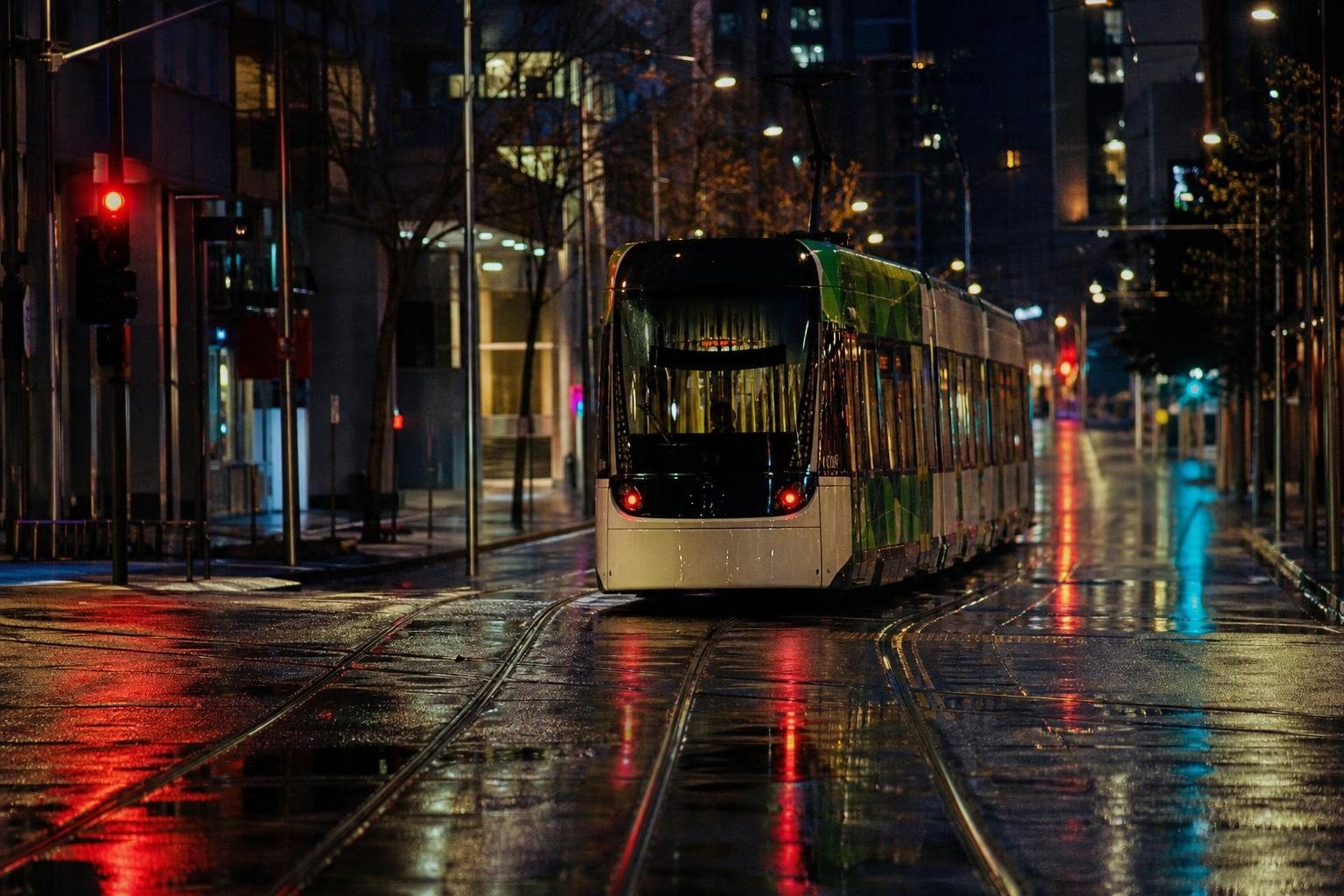 Straßenbahn auf einer regennassen Straße bei Nacht, bunte Lichter spiegeln sich in den Schienen (mit AI erstelltes Bild)