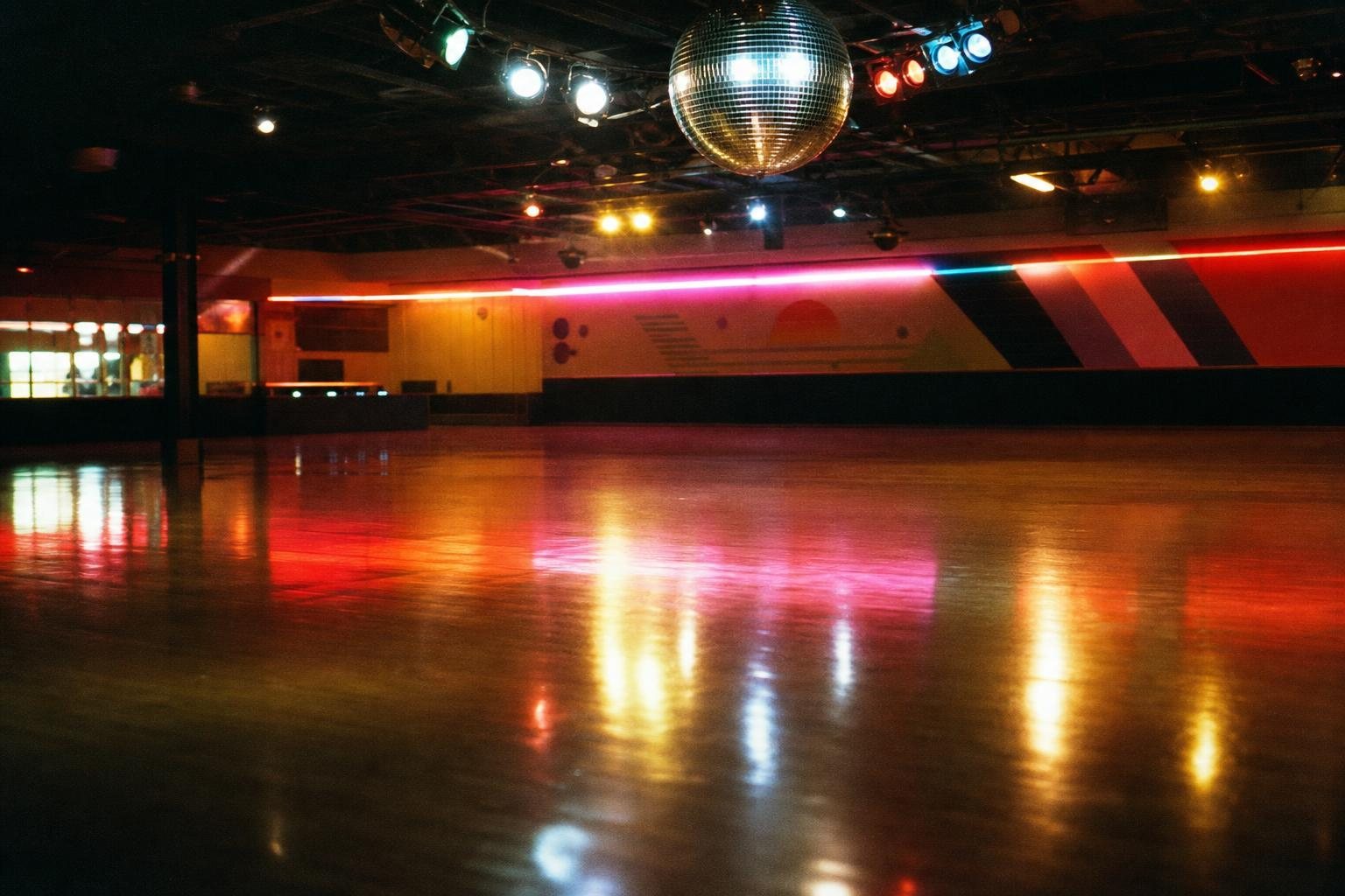 Leere Rollschuhdisco der Achtzigerjahre mit Neonlicht auf glänzendem Boden und Spiegelkugel (mit AI erstelltes Bild)