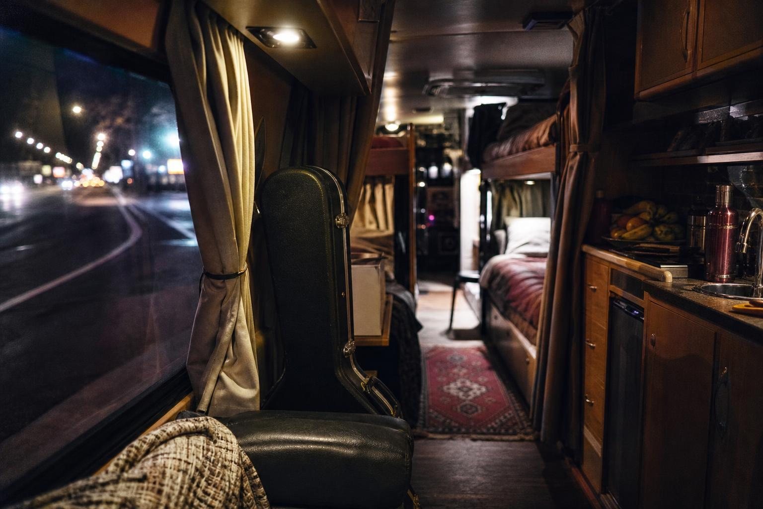 Innenraum eines Tourbusses mit Kojen, Gitarrenkoffer und kleiner Küchenzeile (mit AI erstelltes Bild)