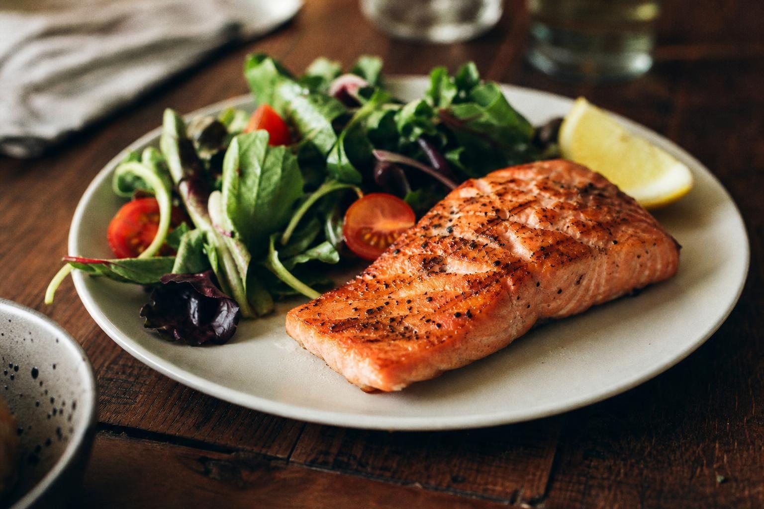 Teller mit gegrilltem Lachs, Blattsalat und Zitrone auf einem Holztisch (mit AI erstelltes Bild)