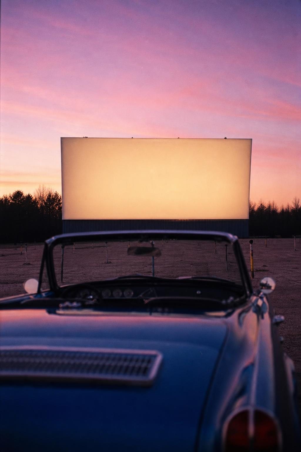 Leeres Autokino in der Dämmerung, ein altes Cabrio vor einer großen hellen Leinwand (mit AI erstelltes Bild)