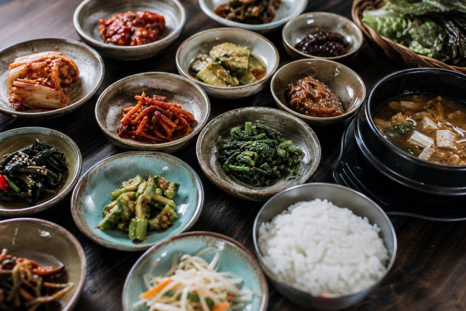 Koreanischer Tisch mit vielen kleinen Beilagen, Kimchi, Reis und Suppe von oben (mit AI erstelltes Bild)