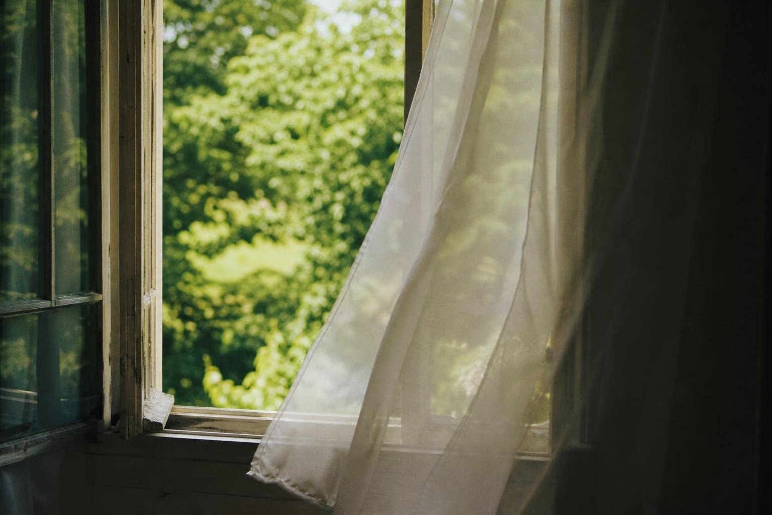 Offenes Fenster mit weißen Vorhängen im frischen Morgenwind, draußen grüne Bäume (mit AI erstelltes Bild)